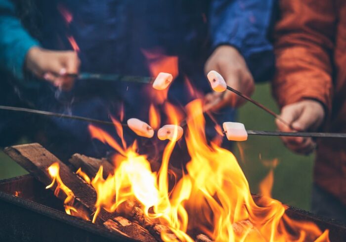 A group of people roast marshmallows over a fire pit. They practice good fall fire safety by keeping a safe distance.