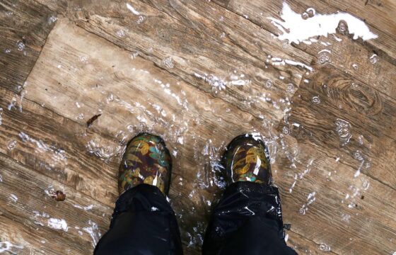 A person's feet standing on flooded hardwood floors