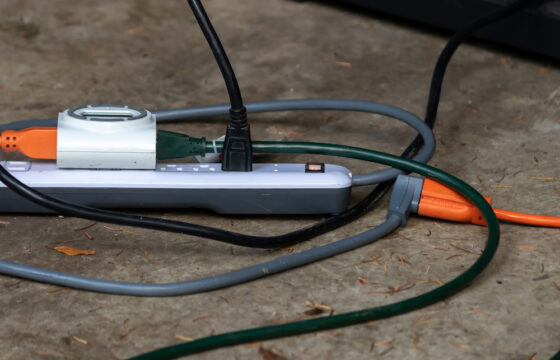 Power strip with multiple outlets and plugs sitting outside on cement.