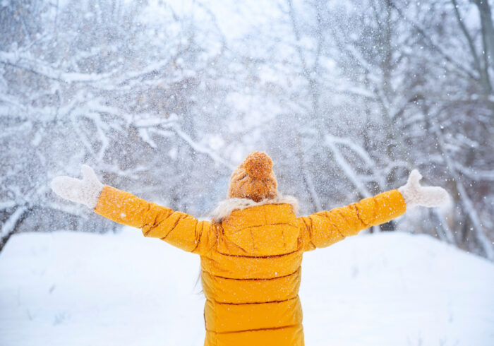 Woman in yellow jacket with back to camera throws snow in the air. Winter safety tips can help ensure you enjoy the snow.