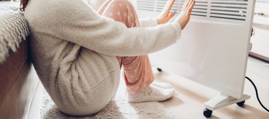 Woman sits next to heater. Tries to conserve heat during winter.