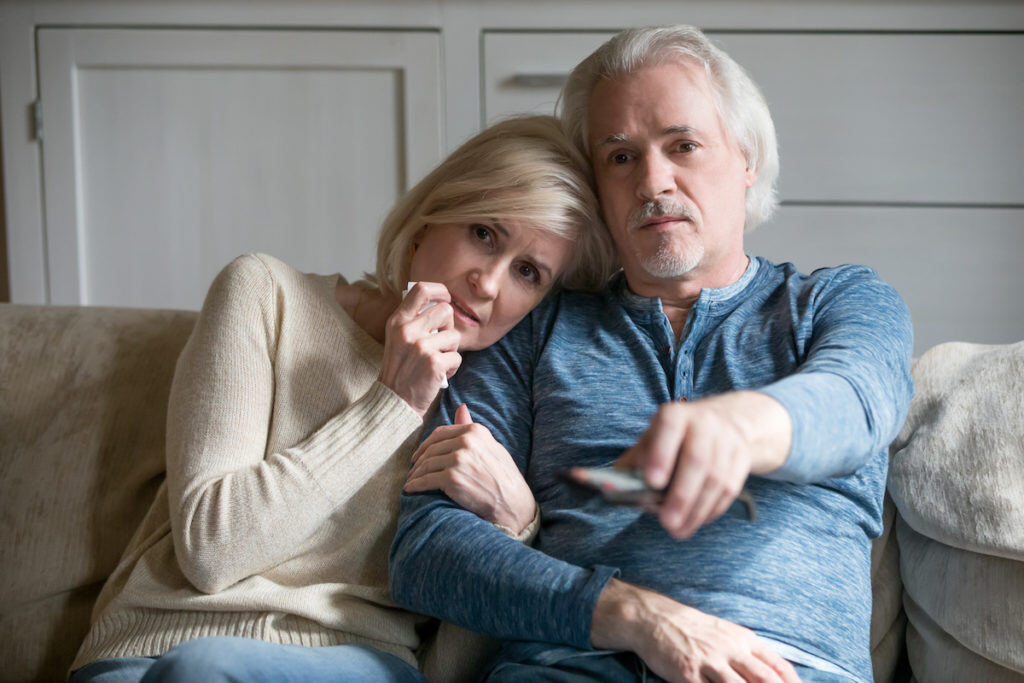 A elderly couple watching TV news about natural disaster in Canada