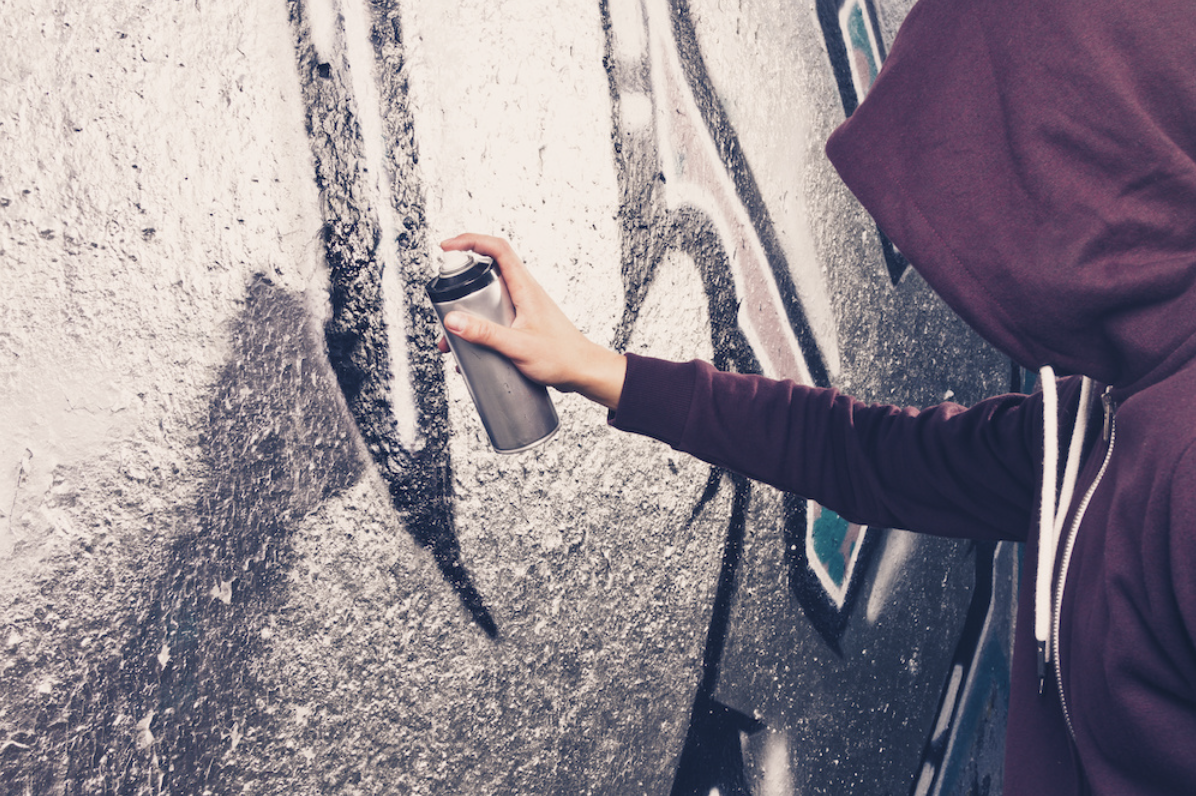 A vandal spraying graffiti on a wall.