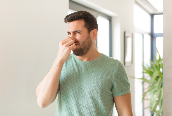 Man in green shirt standing in home holding his nose as if something stinks.