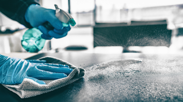 A pair of gloved hands spray a countertop with disinfectant. Disinfecting affected areas is important when it comes to how to get rid of dead mouse smell.