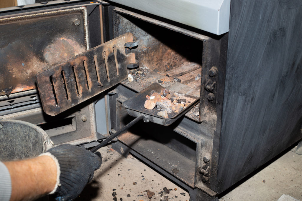 man cleaning the remaining ashes to prevent fireplace smoke in house 