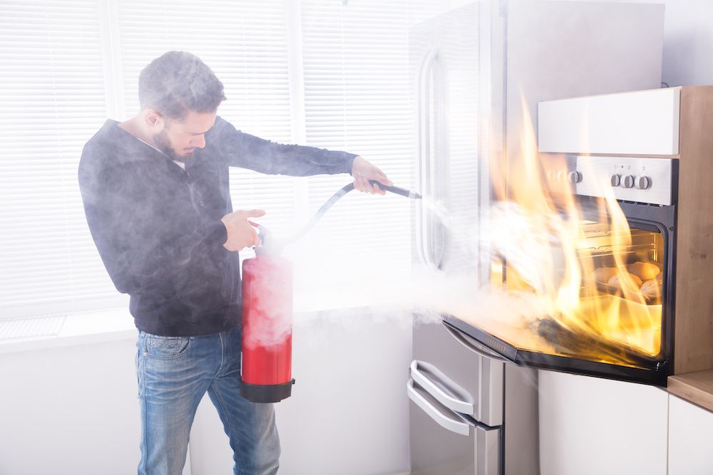A man sprays a fire coming out of an oven with a fire extinguisher. Knowing how to clean up fire extinguisher residue can help in the aftermath.