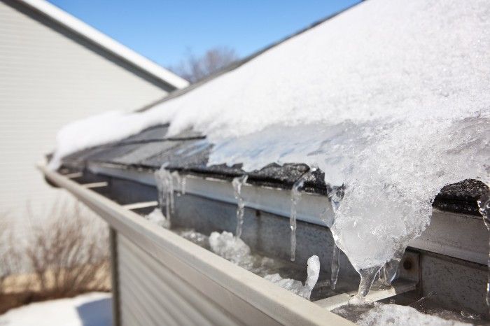 A roof with an ice dam formed on it. Water is trickling off the eaves.